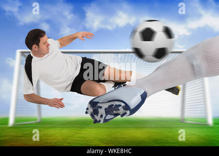 Das zusammengesetzte Bild von Fußballspielern Bekämpfung für die Kugel mit Socke und Boot gegen Fußballplatz und Ziel unter blauem Himmel Stockfoto