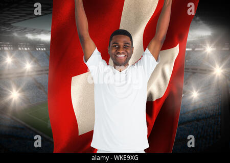 Schöner Fußball fan anfeuern Holding schweizer Flagge gegen große Fußball-Stadion mit Fans in Blau aufgeregt Stockfoto