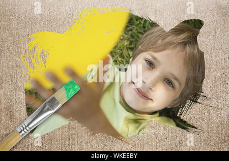 Das zusammengesetzte Bild im kleinen Jungen an Kamera lächelnd mit Pinsel eingetaucht in Grün gegen die verwitterte Oberfläche