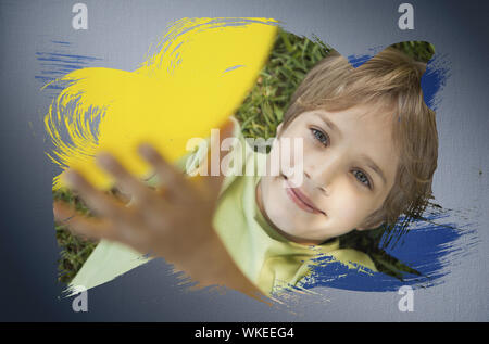 Das zusammengesetzte Bild im kleinen Jungen an Kamera lächelnd mit der blauen Farbe gegen digital erzeugten Grau vignette Hintergrund