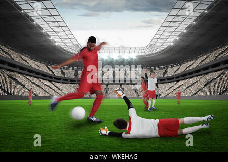 Fußballspieler in rot Kicken gegen große Fußball-Stadion mit Fans in Weiß Stockfoto