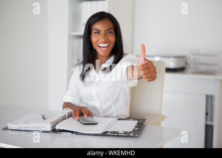 Hübsche Geschäftsfrau, die Daumen bis zu Kamera an Ihrem Schreibtisch in Ihrem Büro Stockfoto