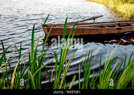 Einen kleinen hölzernen Ruderboot mit einem gebrochenen unten auf einem ruhigen See in der Nähe der Küste. Weißrussland Stockfoto