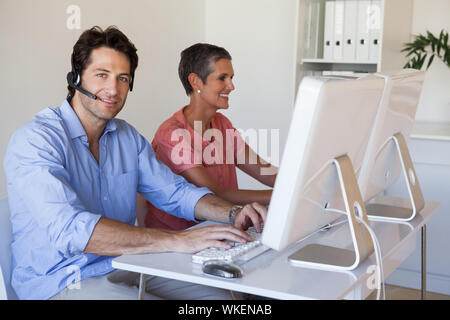 Casual Business Team an der Rezeption einen Computer benutzen, der mit dem Menschen ein Lächeln auf die Kamera im Büro Stockfoto