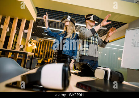 Junge lächelnde Mann und Frau im VR-Brille an Händen mit Augmented Reality aufgeregt. Paar versuchen, VR-Brille und Spaß drinnen Stockfoto