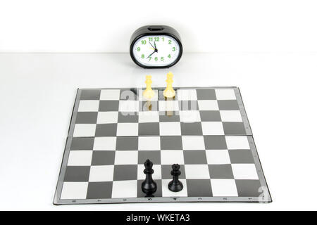 Schachfiguren auf einem karierten Brett mit Uhr Stockfoto