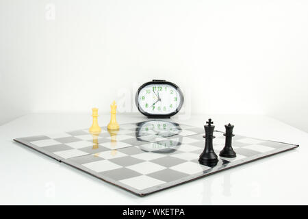 Schachfiguren auf einem karierten Brett mit Uhr Stockfoto