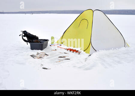 Winter gelb Angeln zelt Feste auf dem Eis mit allen notwendigen Attributen für die Fischerei. Catch roach im Schnee vor dem Zelt liegen. Stockfoto