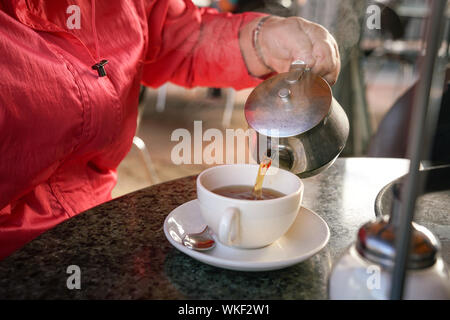 Hand gießen Schwarzer Tee aus Topf in die weiße Tasse Stockfoto