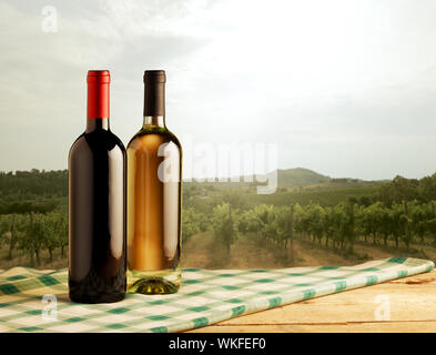 Rote und weiße Weinflaschen auf aufgegebenes Tischdecke und Weinberg im Hintergrund stehen. Stockfoto