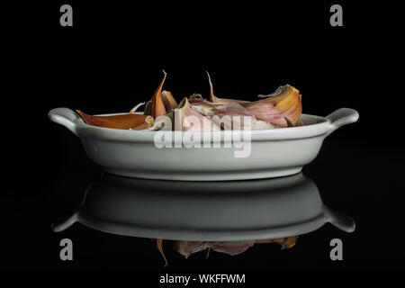 Viele Stücke von organischen Weißer Knoblauch allium sativum in weiße, ovale Keramik Schüssel auf schwarzem Glas isoliert Stockfoto