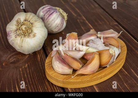 Gruppe von zwei ganze Menge Stücke der organischen Weißer Knoblauch allium sativum auf Bambus Untersetzer auf braunem Holz Stockfoto
