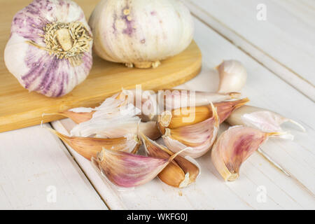 Gruppe von zwei ganze Menge Stücke der organischen Weißer Knoblauch allium sativum auf Bambus Schneidbrett auf weißem Holz Stockfoto
