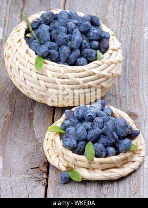Frische reife Geißblatt Beeren in zwei Schalen Korbwaren isoliert auf rustikalen Holzmöbeln Hintergrund Stockfoto
