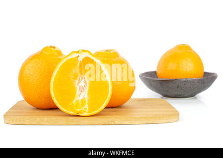 Gruppe von drei ganzen Hälfte der frischen Orange minneola tangelo auf Bambus Schneidebrett in dunklen Keramik Schüssel auf weißem Hintergrund Stockfoto