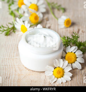 Container mit Sahne und Gänseblümchen auf hölzernen Hintergrund Stockfoto