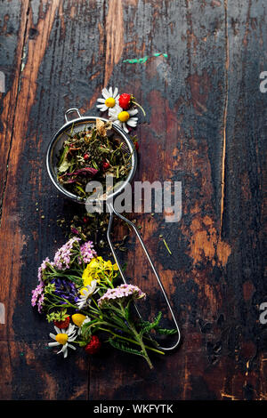 Tee-Stainer mit aromatischen Kräutertee auf Holztisch Hintergrund Stockfoto