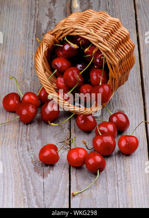 Red Sweet Cherry verstreut aus Weidenkorb auf rustikalen hölzernen Hintergrund Stockfoto