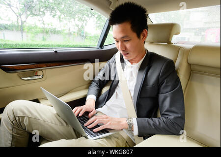 Junge Unternehmer mit Laptop auf dem Rücksitz eines Autos Stockfoto
