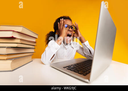 Afro Schule Mädchen schreiend auf Laptop auf Gelb Studio Hintergrund Stockfoto