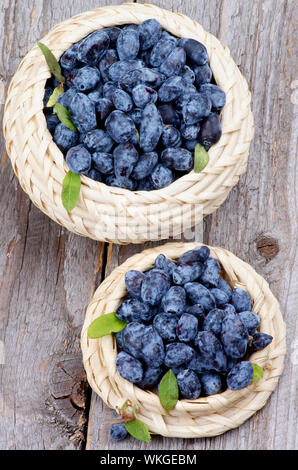 Frische reife Geißblatt Beeren in zwei Schalen Korbwaren isoliert auf rustikalen Holzmöbeln Hintergrund. Ansicht von oben Stockfoto