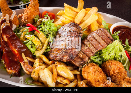 Gesunde platter gemischter Aufschnitt einschließlich gegrilltes Steak, knusprig panierte Hähnchen und Rindfleisch auf einem Bett von frischem grünem Salat serviert mit Französischen Stockfoto