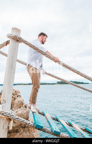 Man Walking durch touristische Suspension Bridge crossing Sea Bay Stockfoto