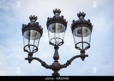 Alte verzierte schmiedeeiserne Lampe mit einem rollbaren Gestell und rechteckigen Glas Laterne auf eine hölzerne Gebäudehülle montiert Stockfoto