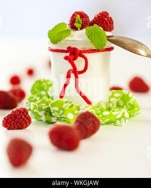 Frische reife Himbeeren serviert mit einem Glas des gesunden Joghurt oder Clotted Cream für ein leckeres Dessert oder Frühstück mit Exemplar Stockfoto