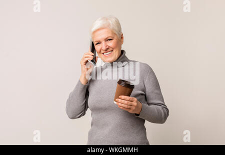 Ältere Frau mit Tasse Kaffee und Reden auf dem Smartphone Stockfoto