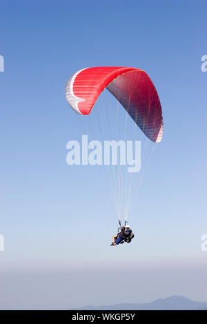 Zwei Personen fliegen mit einem roten Gleitschirm gegen dark blue sky Stockfoto