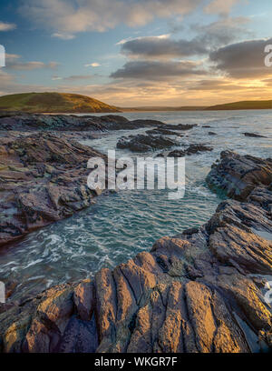 Die Felsen rund um daymer durch die untergehende Sonne beleuchtet. Brea Hügel im Hintergrund und Padstow in der Ferne. Stockfoto