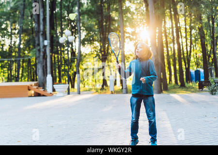 Ein langhaariger schulpflichtige junge in Jeans und einen warmen Pullover spielt eine Badminton Stockfoto