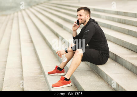 Männliche Athlet sitzt auf der Treppe, ruhen lassen und am Telefon sprechen Stockfoto