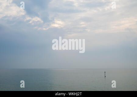 Eine friedliche bewölkter Himmel über ein ruhiges Meer mit einem einzigen groyne Marker. Stockfoto