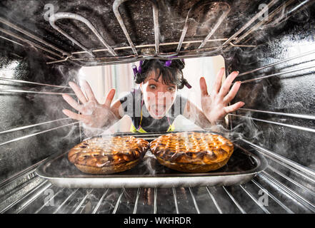 Lustige Hausfrau übersehen Kuchen in den Backofen, damit sie verbrannt hatte, Blick von der Innenseite der Backofen. Hausfrau ratlos und verärgert. Verlierer ist Schicksal! Stockfoto