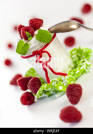 Frische reife Himbeeren serviert mit einem Glas des gesunden Joghurt oder Clotted Cream für ein leckeres Dessert oder Frühstück mit Exemplar Stockfoto