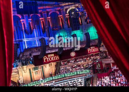 ALBERT HALL INTERIEUR MIT BBC PROMS PERFORMANCE SCHILDERN durch rote Samtvorhänge von Privatbox zum Auditorium, Publikum und Bühne. Royal Albert Hall, Kensington Gore, Kensington, London, Großbritannien Stockfoto