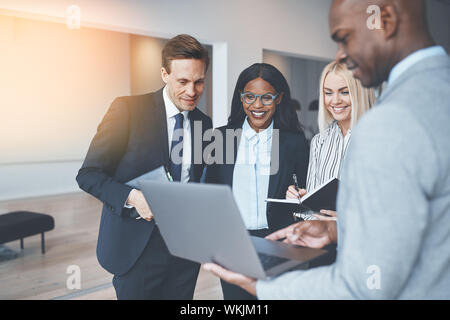 Vielfältige Gruppe von lächelnden Unternehmer diskutieren über ein Laptop während gemeinsam in einem hellen modernen Büro Stockfoto