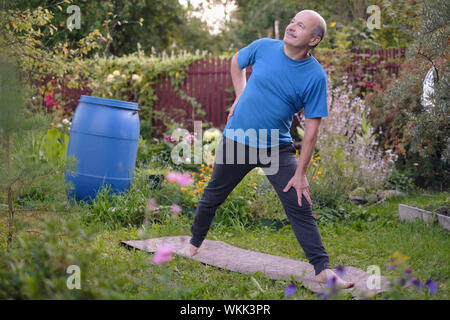 Senior hsipanic Mann, den ich Arbeiten auf der Bank im Garten, Utthita Trikonasana, erweiterte Dreieck darstellen. Yoga für Gesundheit im Alter. Stockfoto