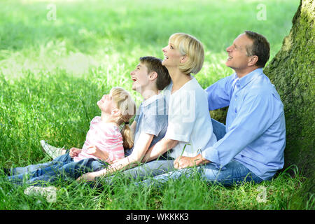 Familie von vier unter Baum sitzt und nachschlagen Stockfoto