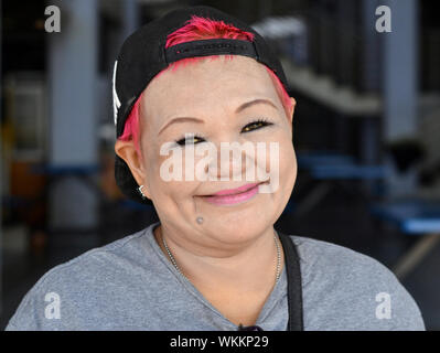 Malaysische chinesische Frau mit rot gefärbten Haaren trägt ein umgekehrt Baseball Cap und unverwechselbaren Augen-Make-up und Lächeln für die Kamera. Stockfoto