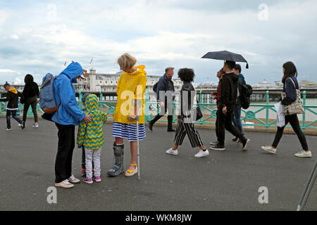 Familie & Besucher die Promenade mit Regenschirm und tragen Regenmäntel an einem regnerischen Sommertag am Pier von Brighton East Sussex England UK KATHY DEWITT Stockfoto