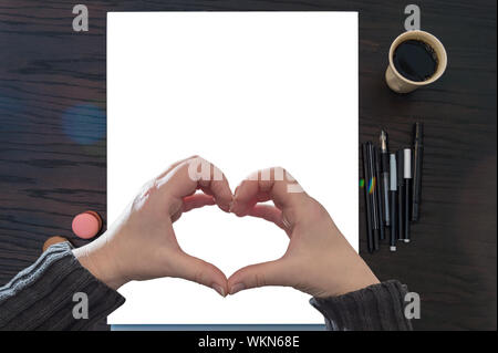 Die beiden Frauen die Hände bilden ein Herz. Für Ihre eigenen Entwürfe Mock auf ein leeres Din A 3-Block. Schwarze Bleistifte, Kaffee und macarons Frame den Block. Stockfoto