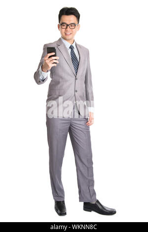 Ganzkörper von jungen asiatischen Geschäftsmann mit Smartphone, SMS und Blick auf das Telefon mit einem Lächeln auf seinem Gesicht, isoliert auf weißem Hintergrund. Stockfoto