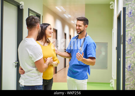 Ein schöner männlicher Arzt Beratung mit einem jungen schwangeren Paare beim Stehen in den Krankenhäusern Flur. Stockfoto