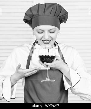 Somellier mit Weinglas. Frau in Cook hat und Schürze. professioneller Koch in der Küche. Küche. Hausfrau Rotwein trinken. glückliche Frau. Grüße an Freunde. Sommelier Prüfung Wein. Das ist perfekter Wein. Stockfoto