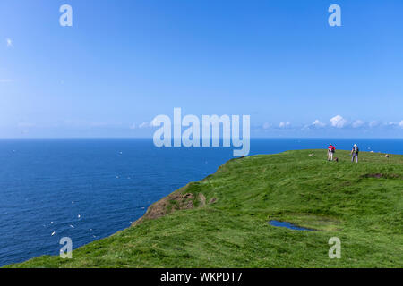 Touristen zu Fuß in der Nähe von Klippen in Unst Hermaness National Nature Reserve, Festland, Shetlandinseln, Schottland, UK Stockfoto