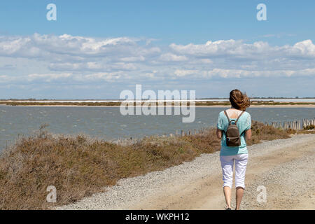 Tausendjährige blonde Mädchen zu Fuß auf der Straße in der Camargue durch Salzwasser Lagunen in der Camarque regionaler Naturpark, Provence Alpes Côte d'Azur, Frankreich Stockfoto