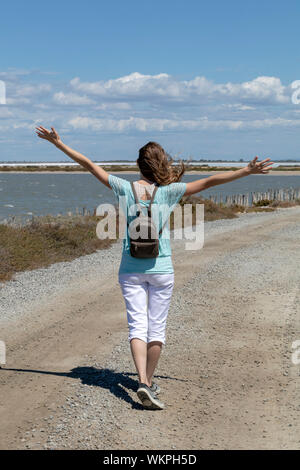 Tausendjährige blonde Mädchen zu Fuß auf der Straße in der Camargue durch Salzwasser Lagunen in der Camarque regionaler Naturpark, Provence Alpes Côte d'Azur, Frankreich Stockfoto